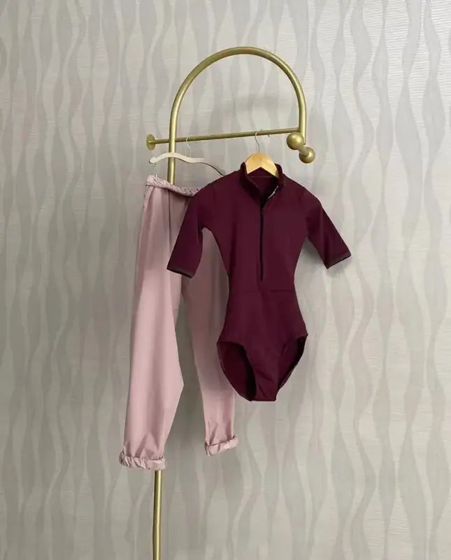 Gold clothing rack displaying a burgundy bodysuit and pink pants.