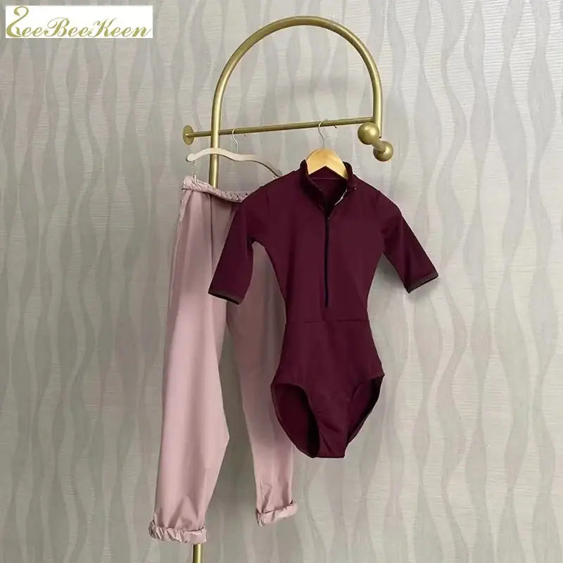 Burgundy bodysuit and pink jogger pants hanging on a brass clothing rack.