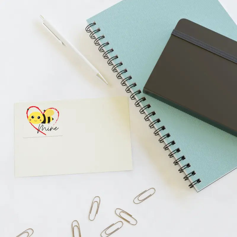 Spiral notebook with a mint green cover alongside paper clips and a bee sticker.