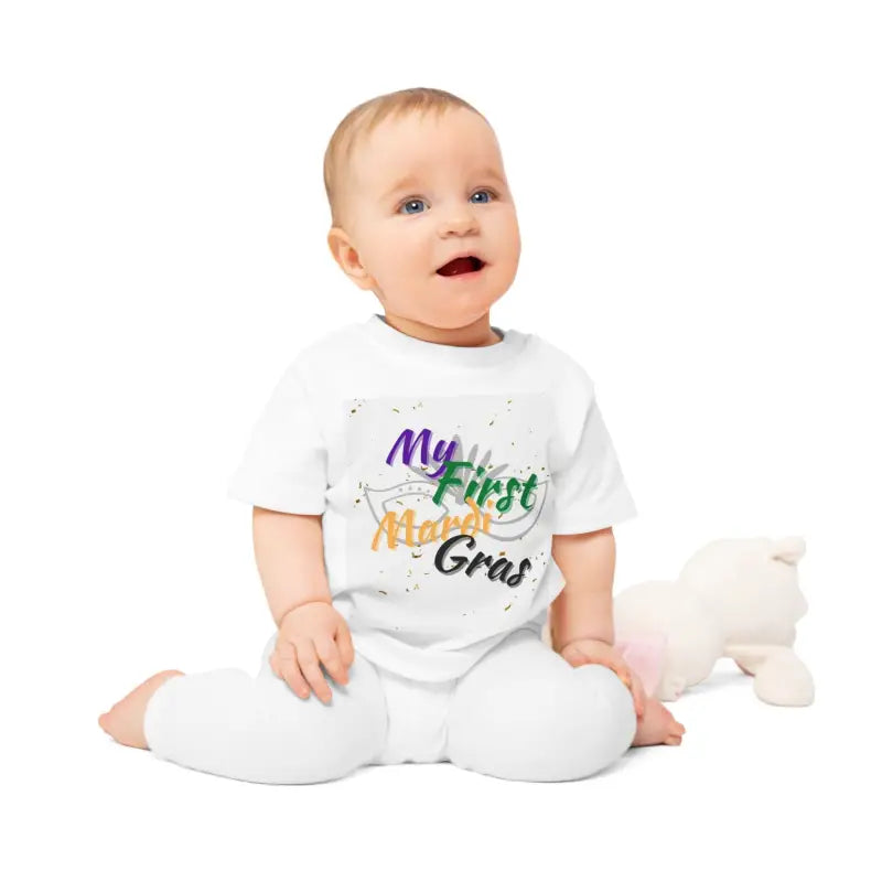A baby wearing a white onesie with ’My First Mardi Gras’ text in colorful letters.