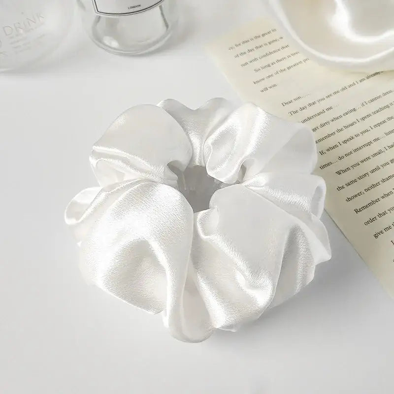 White satin hair scrunchie with a gathered, ruffled texture.