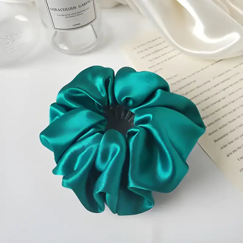 Emerald green satin scrunchie with gathered fabric folds.