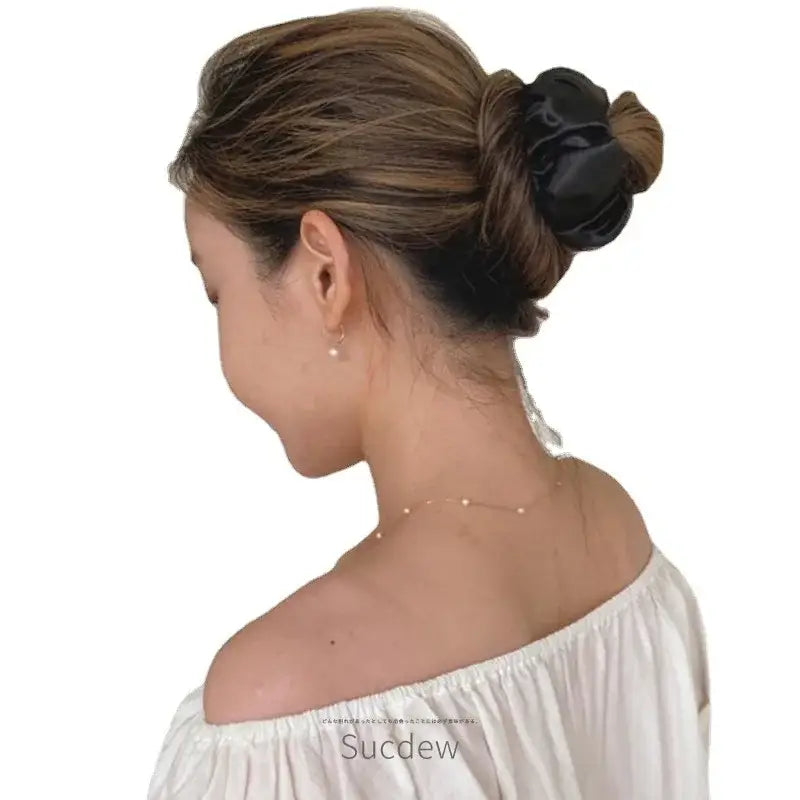 Elegant updo hairstyle with a black hair accessory and off-shoulder white top.