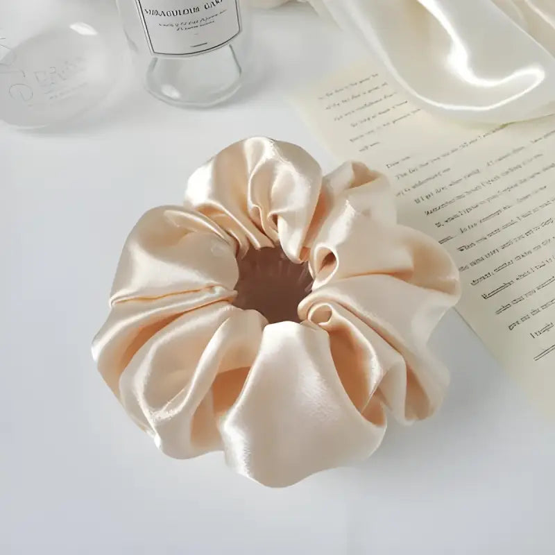 Peach-colored satin hair scrunchie with gathered fabric folds.