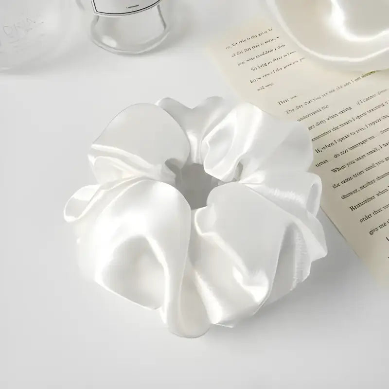 White satin hair scrunchie with a gathered, ruffled texture.