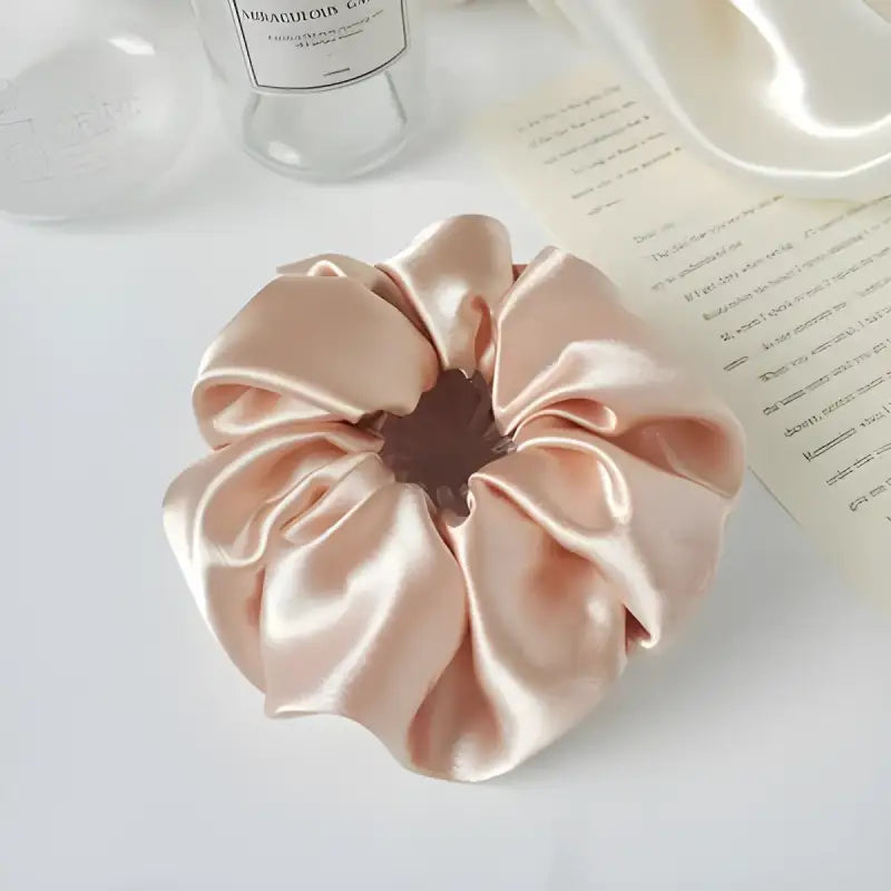 Silky pink satin scrunchie with gathered fabric folds.