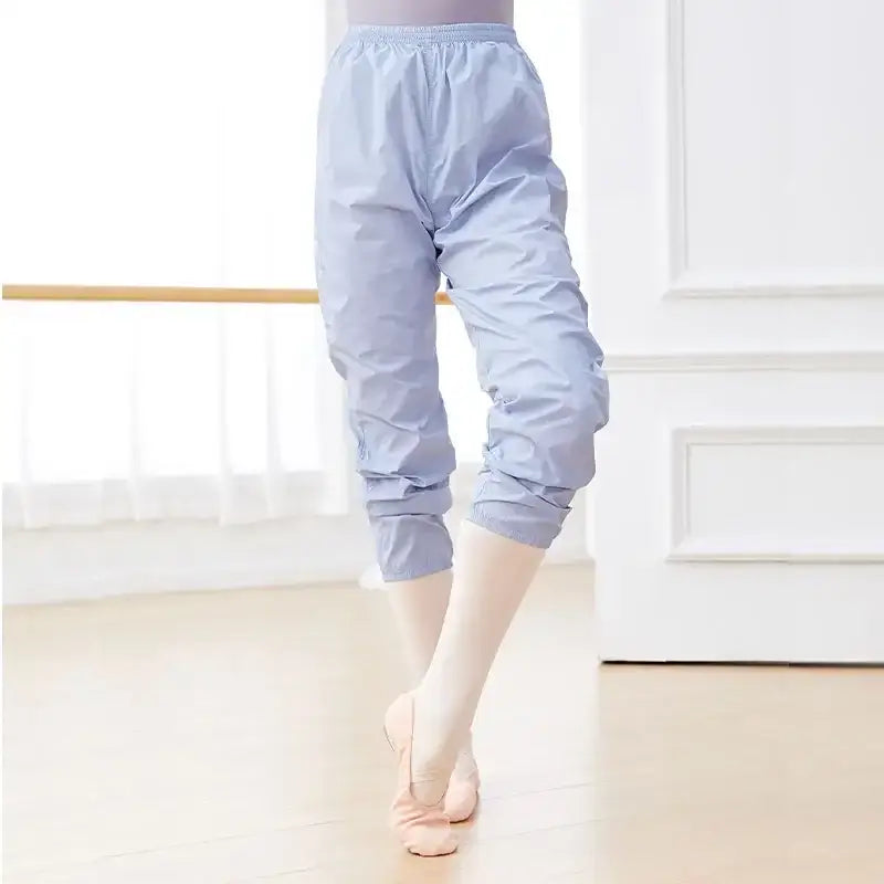Light blue dance warm-up pants with elastic cuffs worn over ballet tights and pointe shoes.