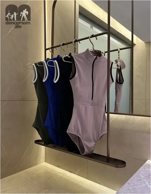 Sleeveless leotards in black, blue, and pink hanging on a clothing rack.