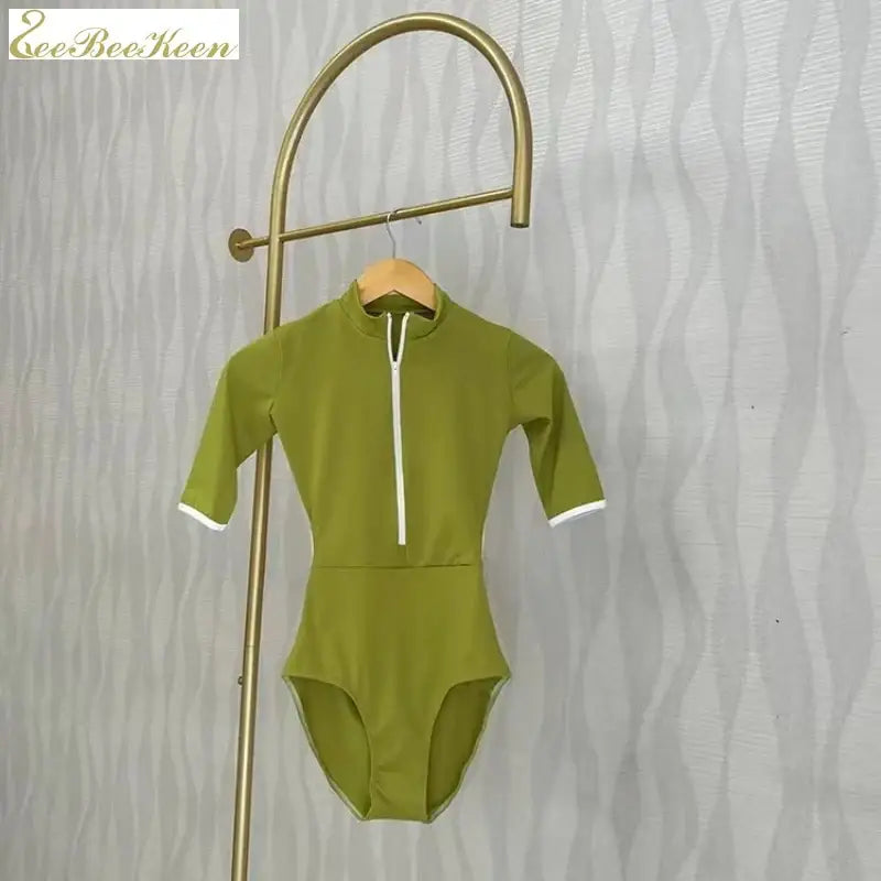 Olive green half-zip bodysuit with white trim and short sleeves hanging on a brass display hook.