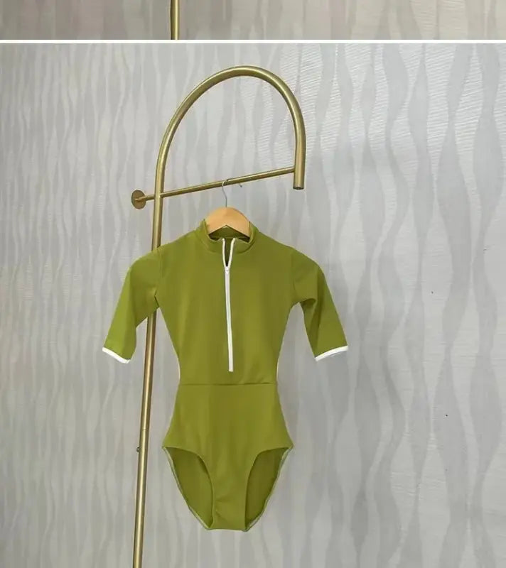 Olive green half-zip swimsuit with white trim hanging on a brass display hook.