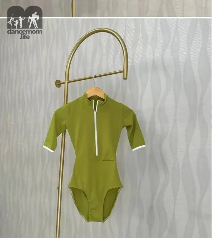 Olive green half-zip swimsuit with white trim hanging on a brass display hook.