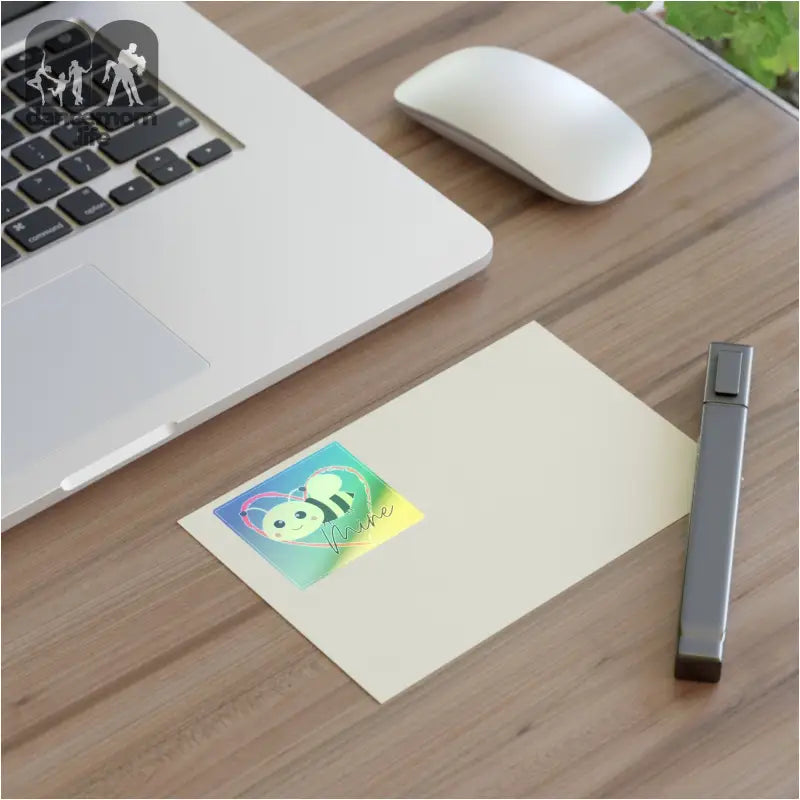 Holographic bee sticker on a piece of paper next to a laptop and mouse.