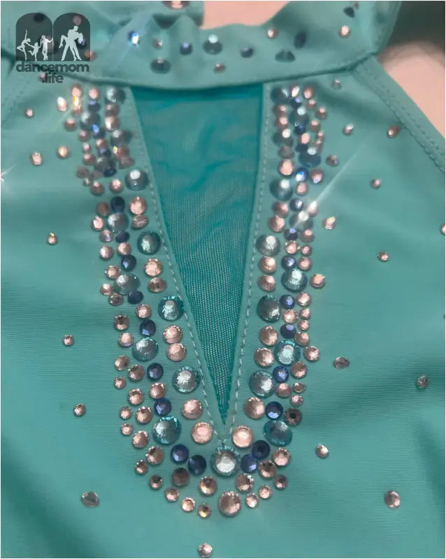 Turquoise garment with a V-shaped neckline adorned with rhinestones and pearls.