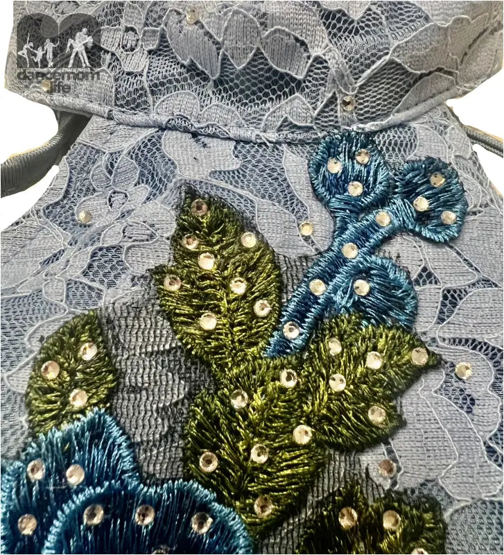 Delicate lace fabric adorned with embroidered floral designs in blue and green, accented with pearl-like beads.