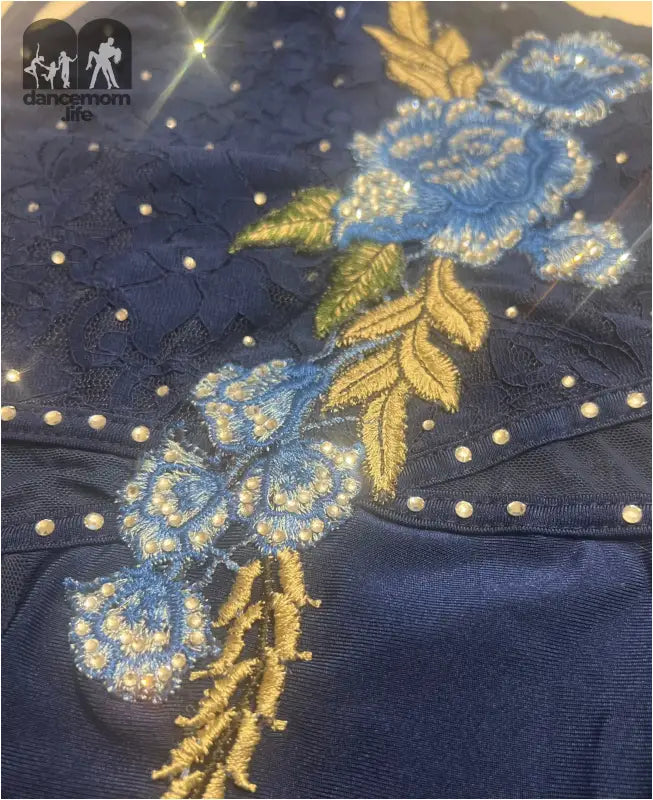 Intricate floral embroidery in blue and gold thread on dark fabric.