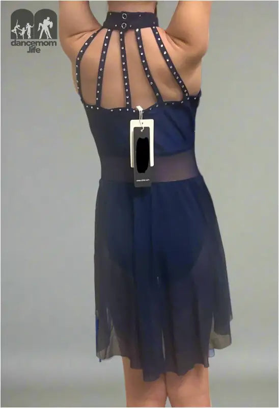 Navy blue cocktail dress with a strappy, studded back design and sheer overlay.