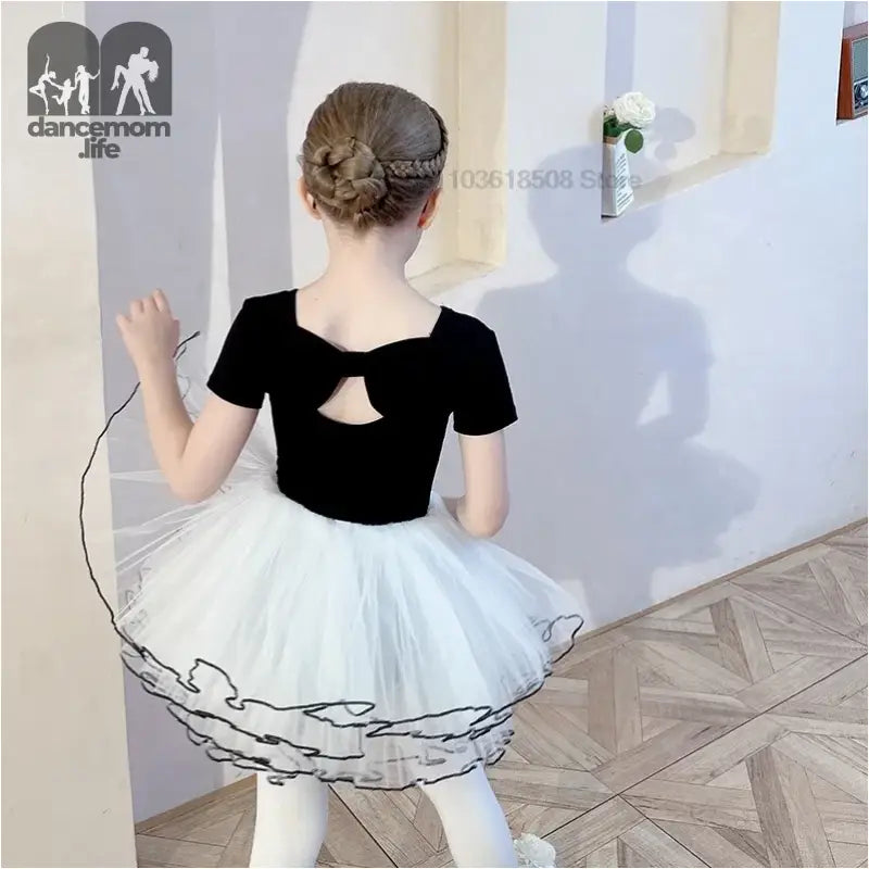 Ballet dancer wearing a black leotard with short sleeves and white tutu skirt.