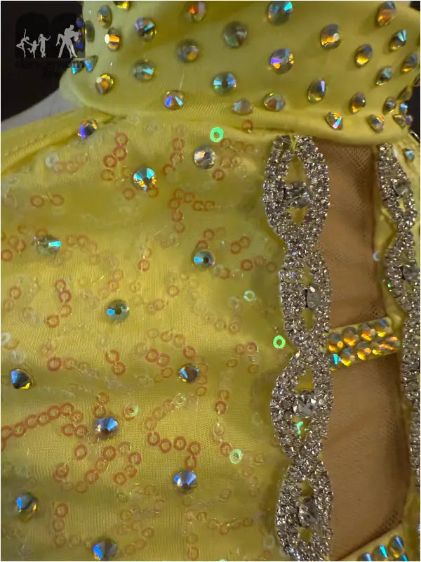 Yellow fabric adorned with iridescent crystals and a rhinestone trim pattern.