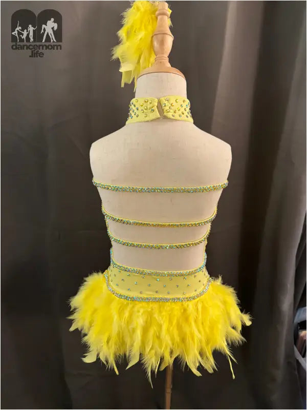 Yellow feathered dance costume with rhinestone straps on a dress form mannequin.