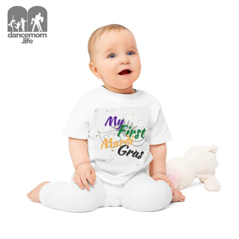 A baby wearing a white onesie with ’My First Mardi Gras’ text in colorful letters.