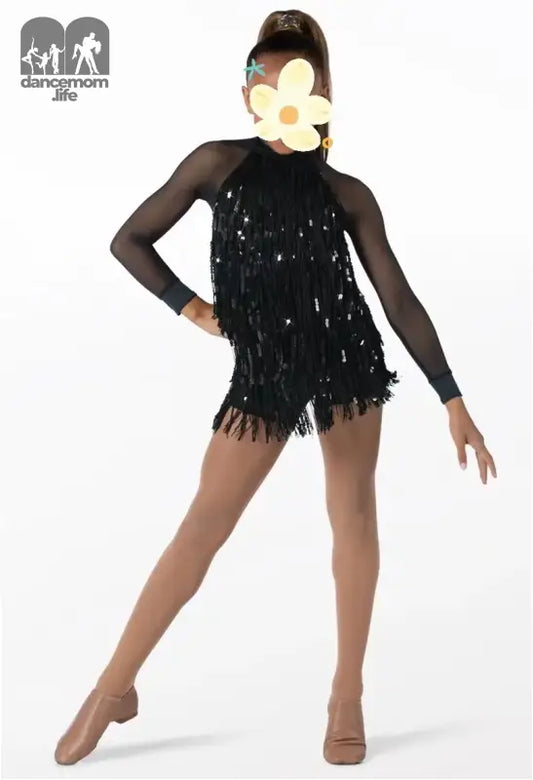 Dancer wearing a black sequined costume with sheer sleeves and a large white flower accessory.