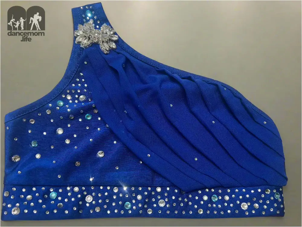 Royal blue one-shoulder top adorned with sparkling rhinestones and a decorative floral appliqué.