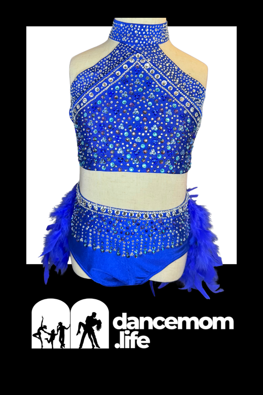 A vibrant royal blue dance outfit featuring a high-necked, beaded halter top and matching shorts adorned with shimmering rhinestones and fluffy feather trim.