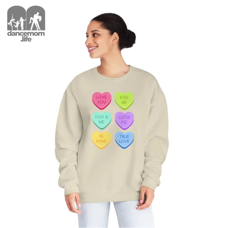 Beige sweatshirt featuring colorful candy heart designs with messages printed on them.